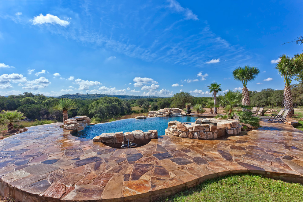Cette photo montre une très grande piscine à débordement et arrière chic sur mesure avec un point d'eau et des pavés en pierre naturelle.