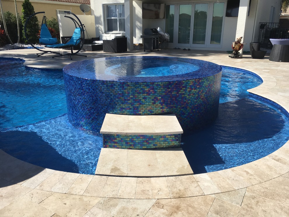 Diseño de piscina natural exótica grande a medida en patio trasero con adoquines de piedra natural