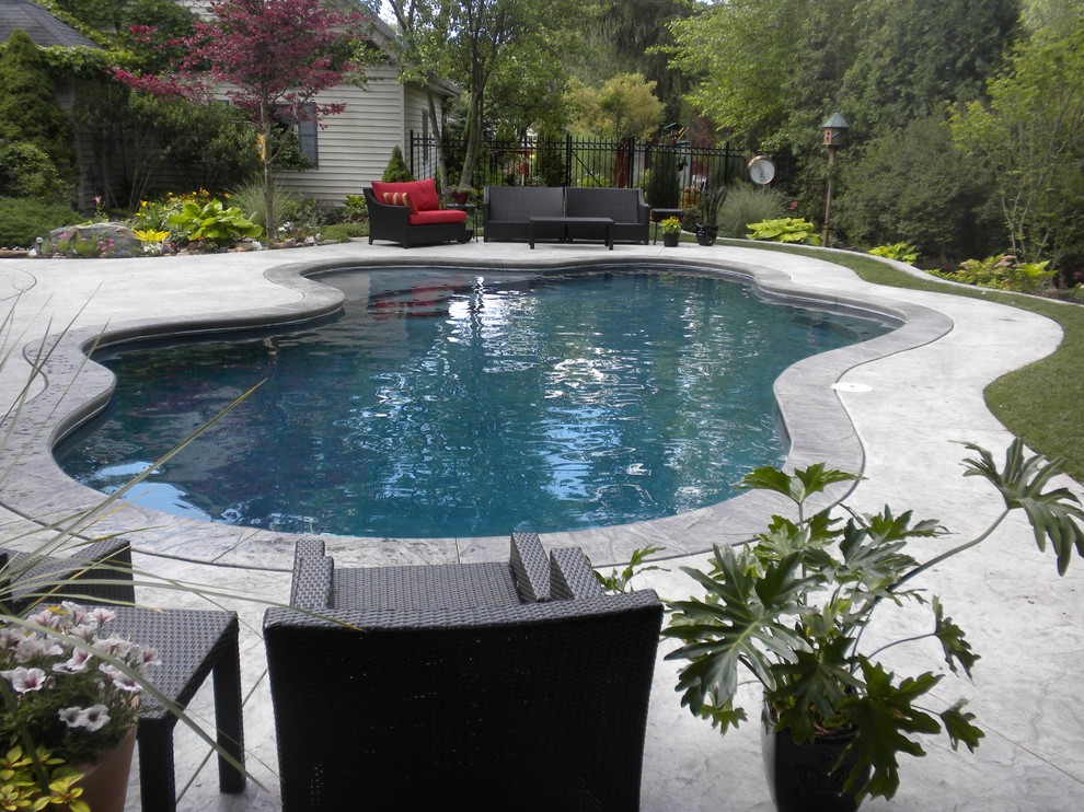 Imagen de piscina clásica de tamaño medio a medida en patio trasero con suelo de hormigón estampado
