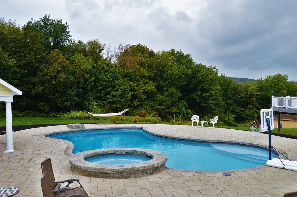Ispirazione per una piscina naturale classica personalizzata di medie dimensioni e dietro casa con una vasca idromassaggio e pavimentazioni in cemento