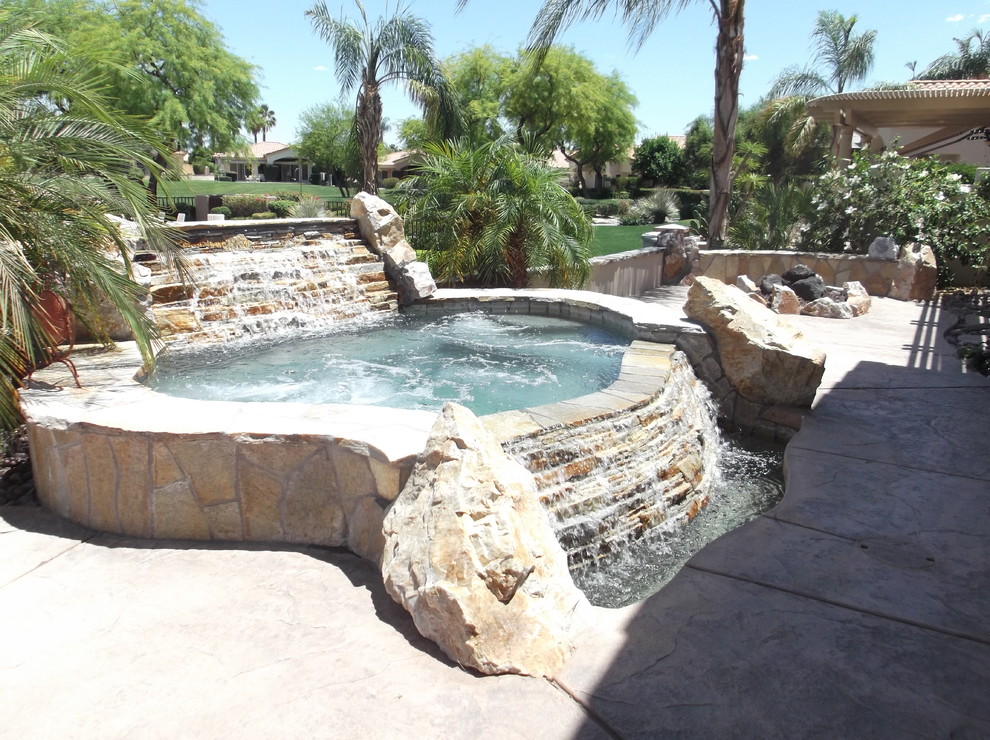Ejemplo de piscina con fuente alargada tropical grande a medida en patio trasero con losas de hormigón