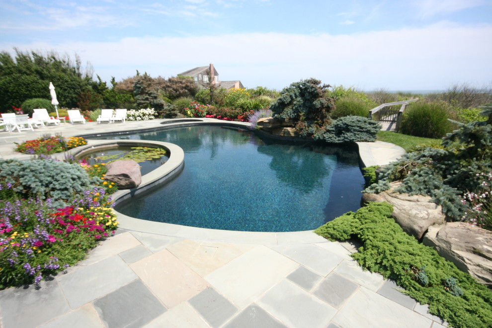 Ejemplo de piscina natural marinera grande tipo riñón en patio trasero con adoquines de piedra natural