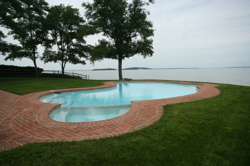 Bild på en stor maritim njurformad pool på baksidan av huset, med spabad och marksten i tegel