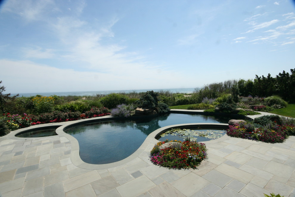 Modelo de piscina natural costera grande tipo riñón en patio trasero con adoquines de piedra natural