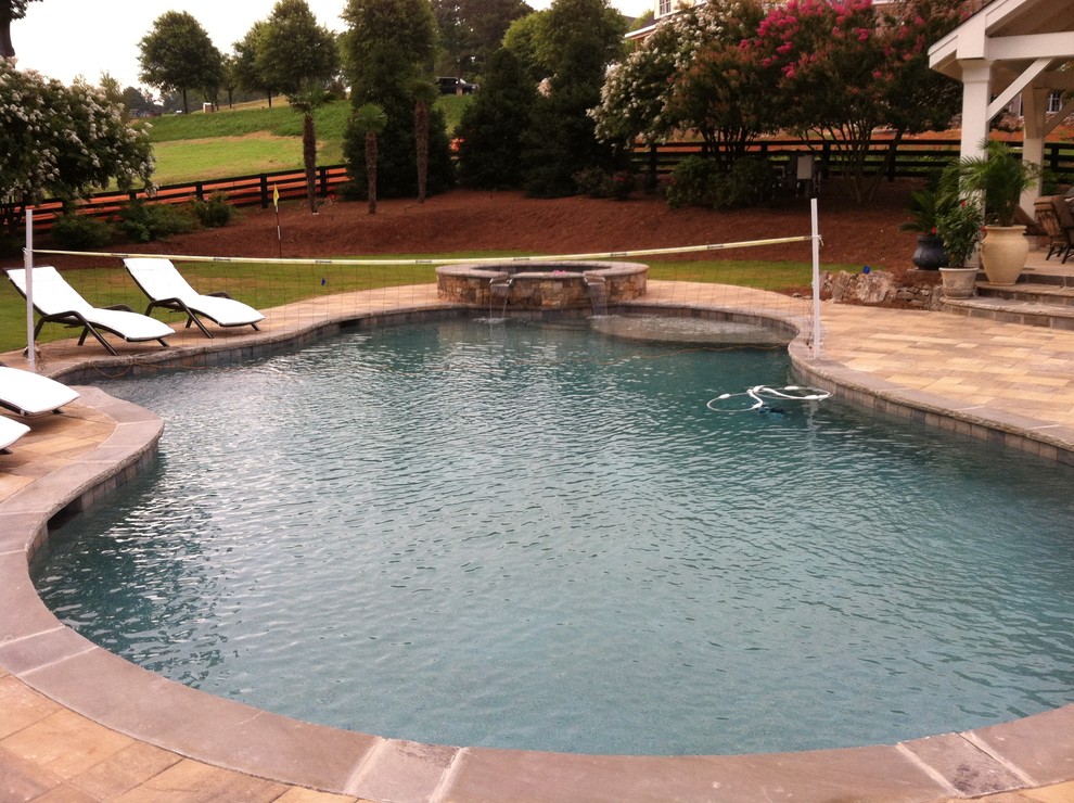 Immagine di una grande piscina tradizionale personalizzata dietro casa con fontane e pavimentazioni in pietra naturale