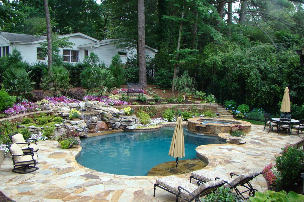 Cette image montre une grande piscine arrière traditionnelle sur mesure avec un bain bouillonnant et des pavés en pierre naturelle.