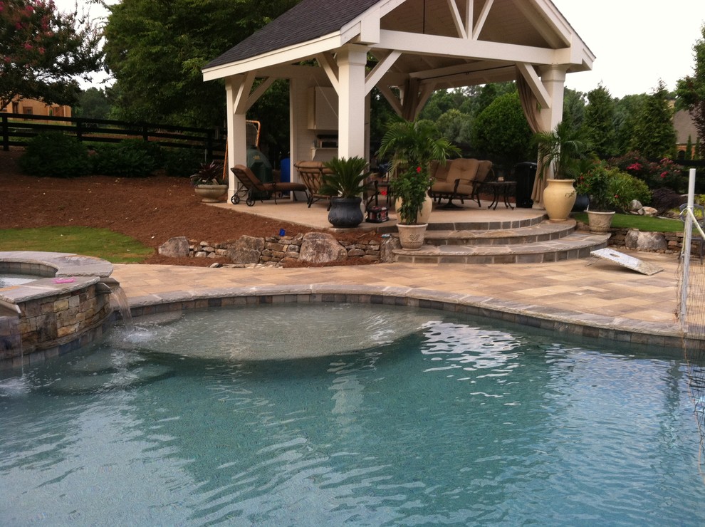 Idée de décoration pour une grande piscine arrière tradition sur mesure avec un point d'eau et des pavés en pierre naturelle.