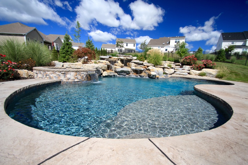 Foto på en stor funkis pool på baksidan av huset, med spabad och stämplad betong