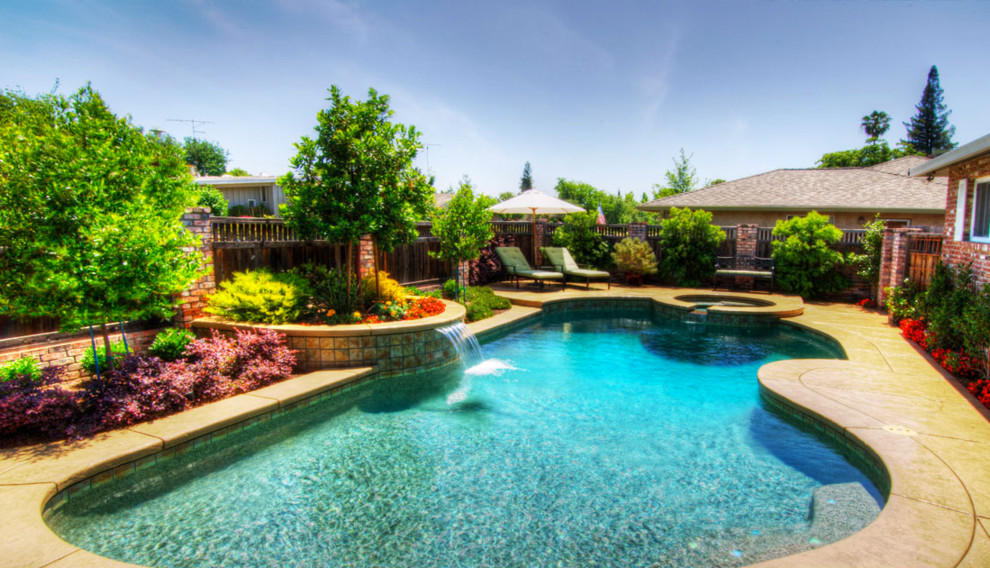 Foto på en stor tropisk pool på baksidan av huset, med en fontän och betongplatta
