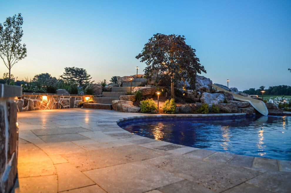 Ejemplo de piscina natural rústica grande a medida en patio trasero con paisajismo de piscina y adoquines de piedra natural