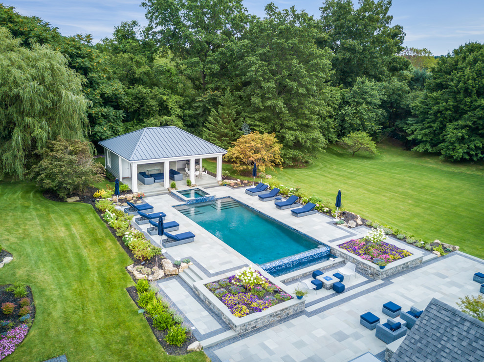 Immagine di una grande piscina a sfioro infinito classica rettangolare dietro casa con una dépendance a bordo piscina e pavimentazioni in pietra naturale