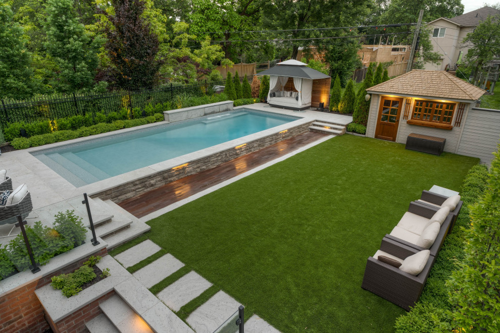 На фото: прямоугольный бассейн среднего размера на заднем дворе в стиле неоклассика (современная классика) с домиком у бассейна и покрытием из каменной брусчатки с