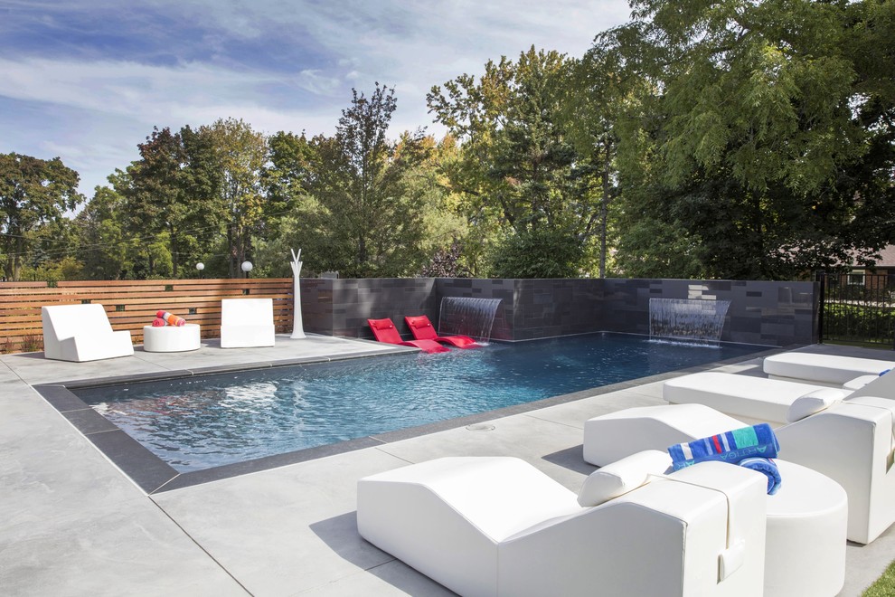 Modelo de casa de la piscina y piscina alargada de tamaño medio rectangular en patio trasero con suelo de hormigón estampado