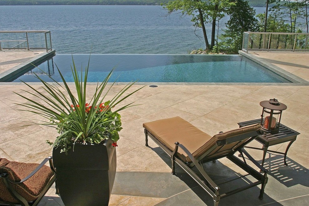 This is an example of a medium sized contemporary back rectangular infinity swimming pool in Toronto with natural stone paving.