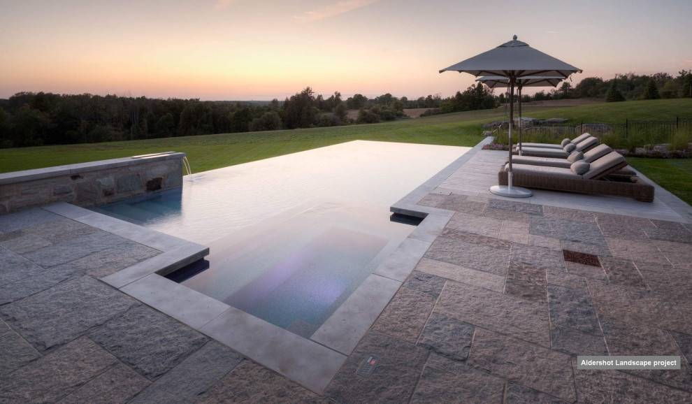 Foto de piscina infinita tradicional renovada de tamaño medio rectangular en patio trasero con paisajismo de piscina y adoquines de piedra natural