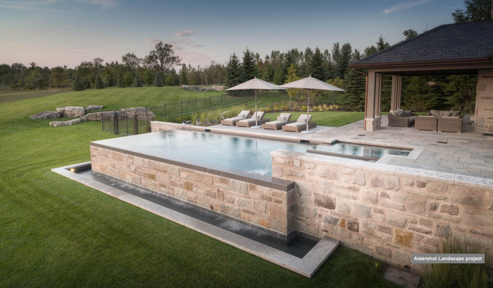 Ejemplo de piscina infinita clásica renovada de tamaño medio rectangular en patio trasero con paisajismo de piscina y adoquines de piedra natural