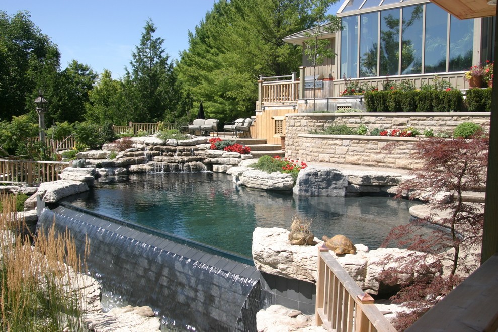 Mittelgroßer Moderner Infinity-Pool hinter dem Haus in individueller Form mit Wasserspiel und Natursteinplatten in Sonstige