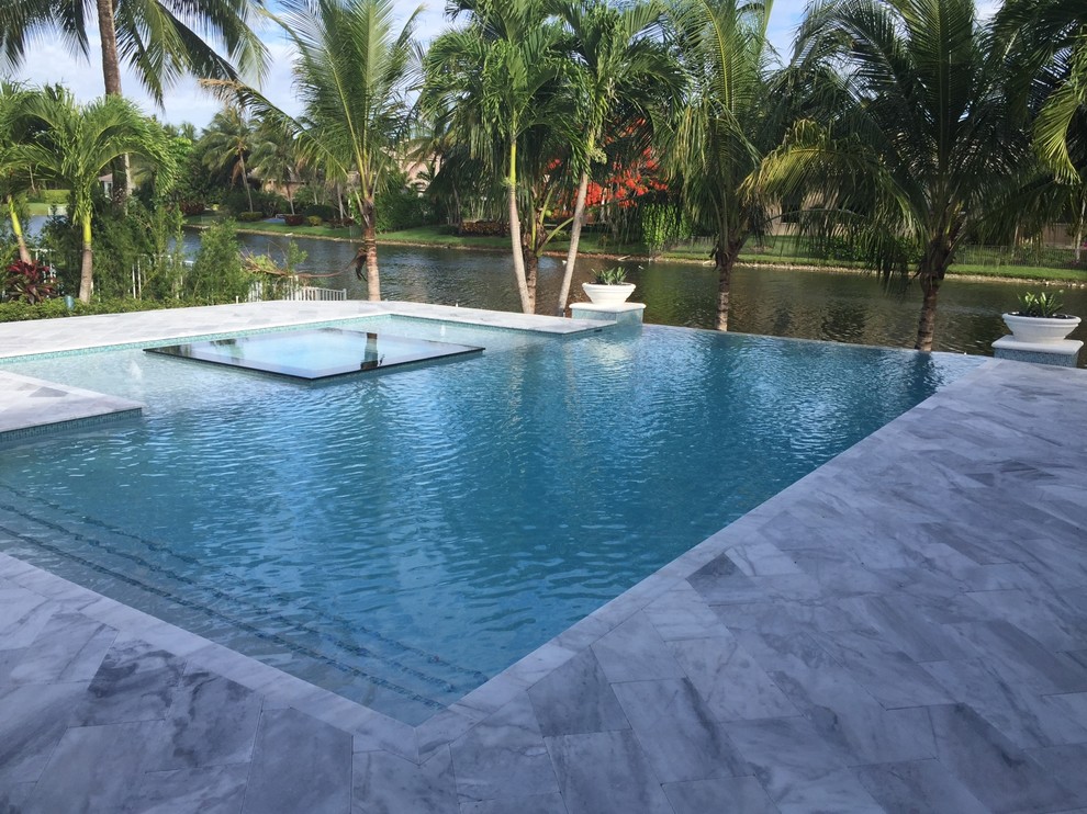 Пример оригинального дизайна: большой бассейн-инфинити произвольной формы на заднем дворе в стиле модернизм с джакузи и покрытием из каменной брусчатки