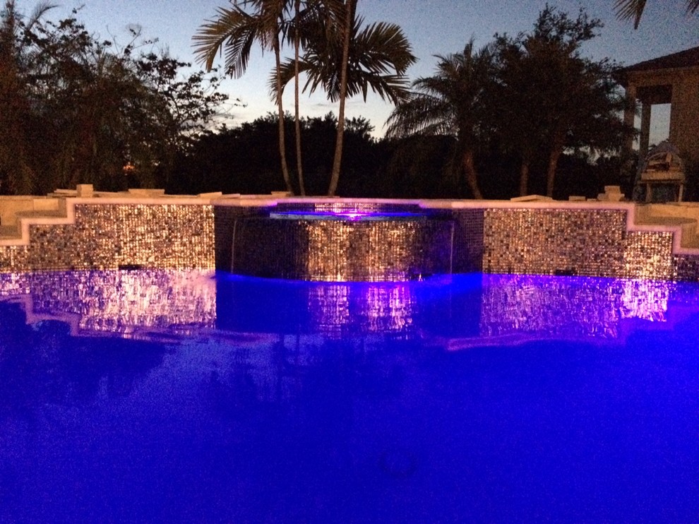 На фото: большой бассейн произвольной формы на заднем дворе в стиле модернизм с джакузи и покрытием из каменной брусчатки с