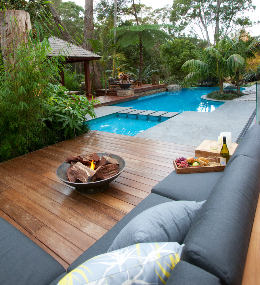 Modelo de casa de la piscina y piscina natural tropical de tamaño medio a medida en patio trasero con adoquines de piedra natural