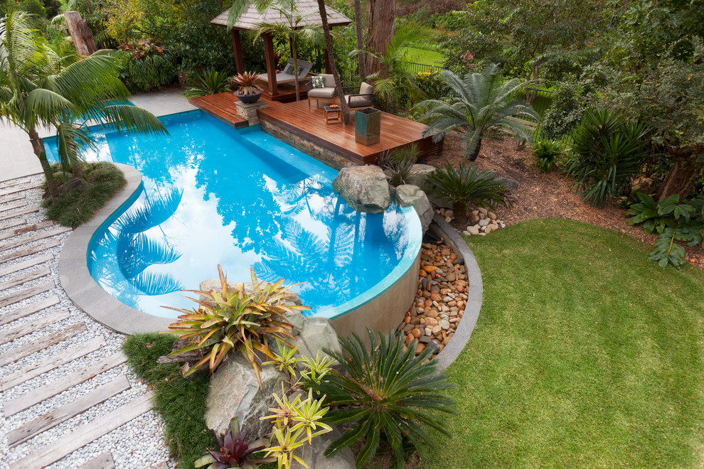 Inspiration för en mellanstor tropisk anpassad baddamm på baksidan av huset, med poolhus och naturstensplattor