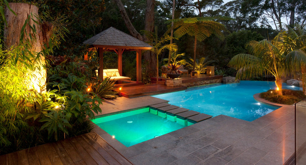 Esempio di una piscina naturale tropicale personalizzata di medie dimensioni e dietro casa con una dépendance a bordo piscina e pavimentazioni in pietra naturale