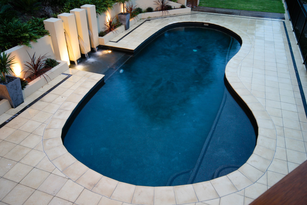 Large contemporary back custom shaped swimming pool in Brisbane with a water feature and concrete paving.