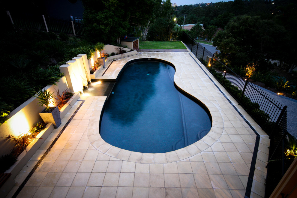 This is an example of a large contemporary back custom shaped natural swimming pool in Brisbane with a water feature and concrete paving.