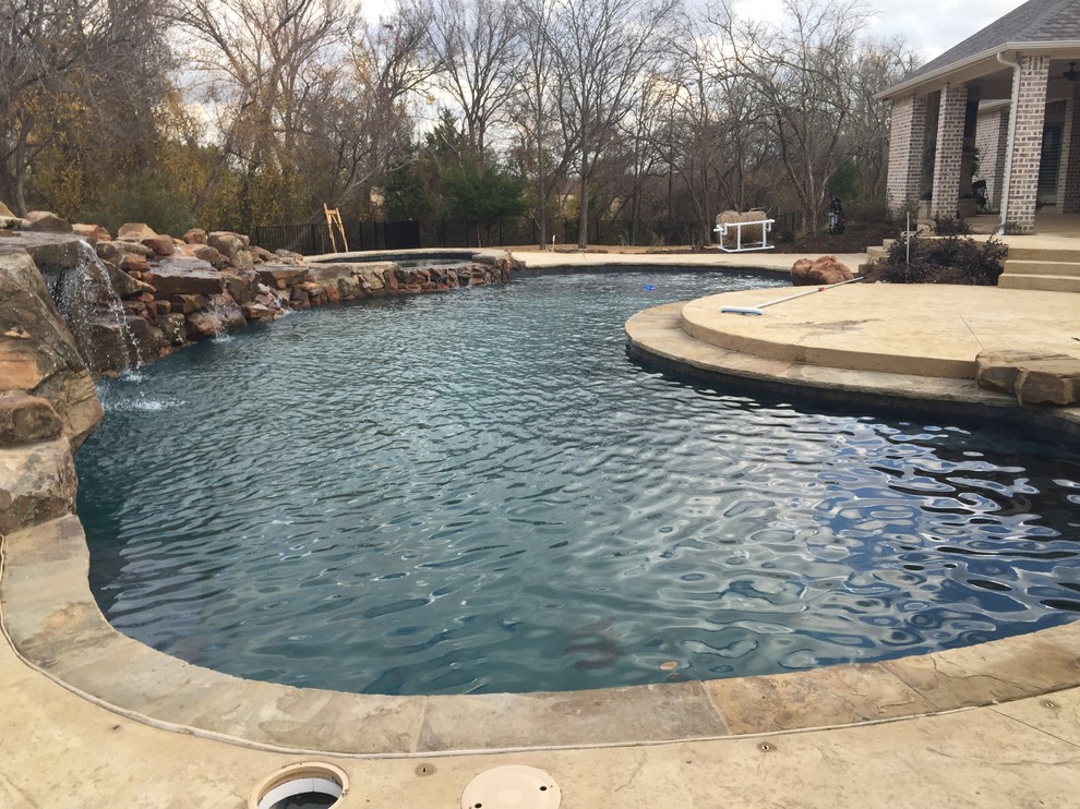 This is an example of a large contemporary back kidney-shaped natural swimming pool in Dallas with a water feature and concrete slabs.