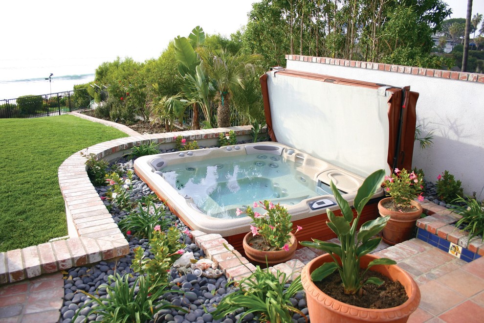 Diseño de piscinas y jacuzzis elevados tropicales rectangulares en patio trasero con adoquines de ladrillo