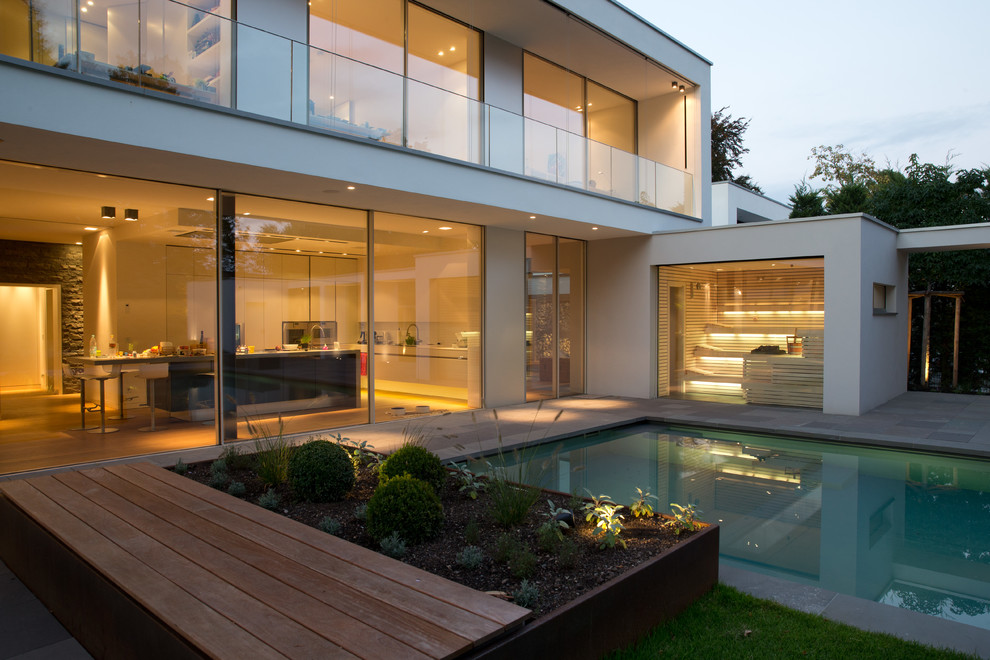 Large contemporary side rectangular swimming pool in Cologne with natural stone paving and a pool house.