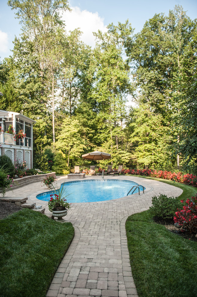 Imagen de piscina clásica grande tipo riñón en patio trasero con adoquines de hormigón