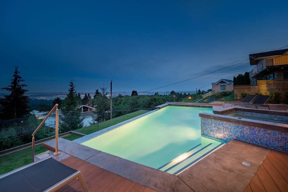 Aménagement d'une piscine à débordement et arrière contemporaine sur mesure avec un bain bouillonnant et une terrasse en bois.