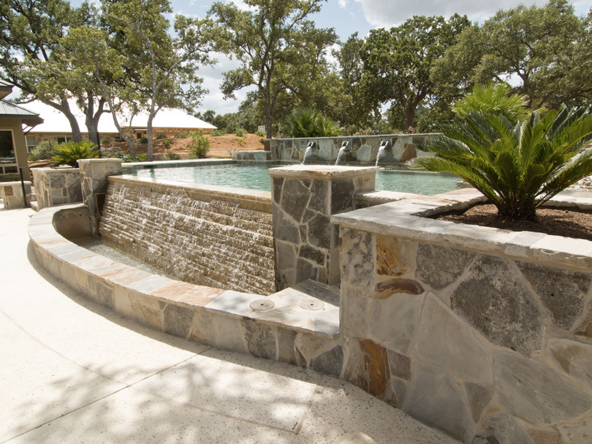 Medium sized mediterranean back custom shaped infinity swimming pool in Austin with a water feature and concrete paving.