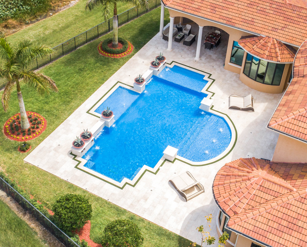 Photo of an expansive traditional back custom shaped swimming pool in Miami with a water feature and natural stone paving.
