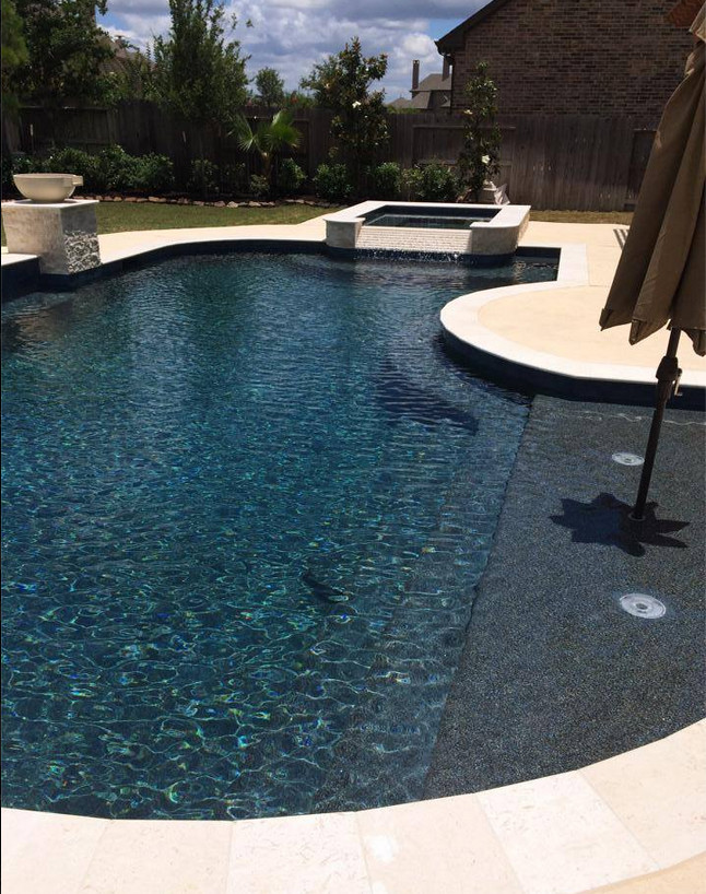 Large contemporary back custom shaped natural swimming pool in Houston with a water feature and natural stone paving.