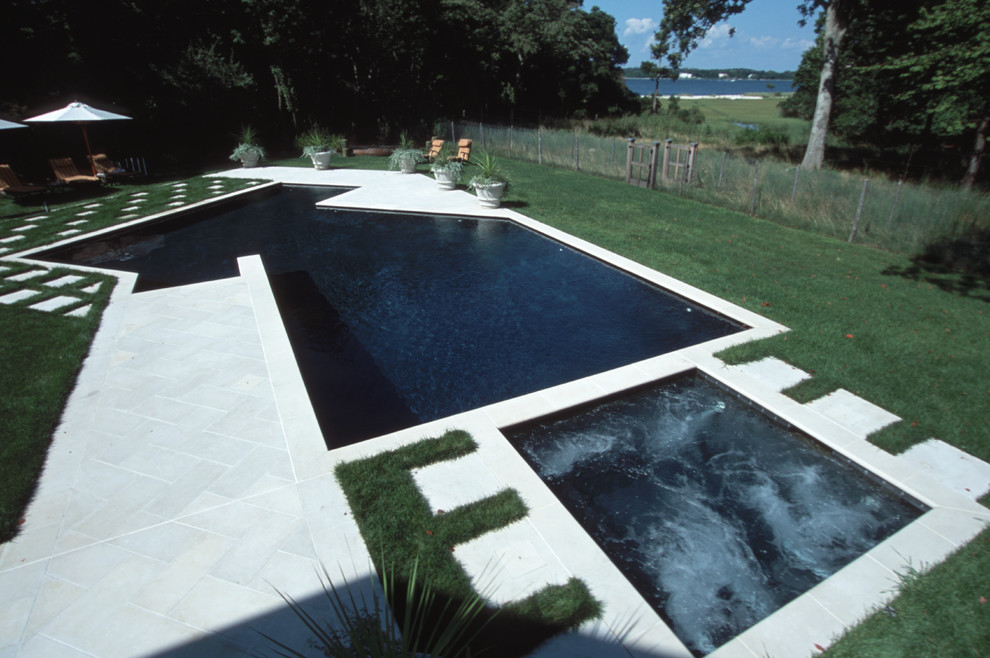 Idée de décoration pour une grande piscine arrière design sur mesure avec un bain bouillonnant et des pavés en pierre naturelle.