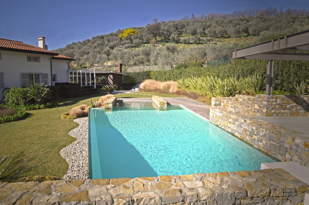 Diseño de piscina infinita contemporánea grande rectangular en patio trasero con adoquines de piedra natural