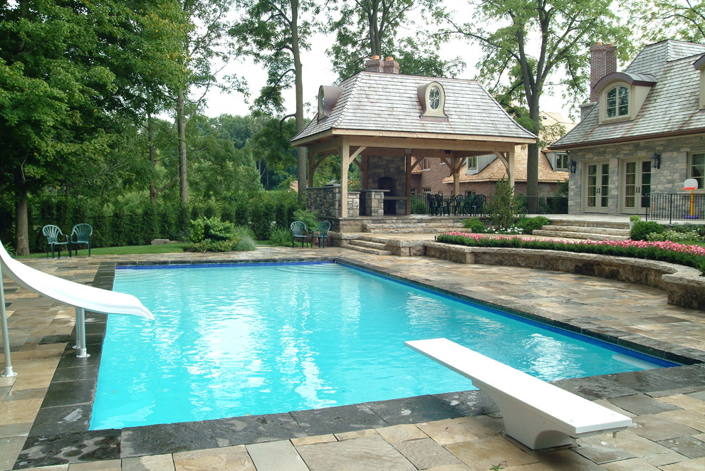 На фото: большой прямоугольный бассейн на заднем дворе в классическом стиле с водной горкой и покрытием из каменной брусчатки с