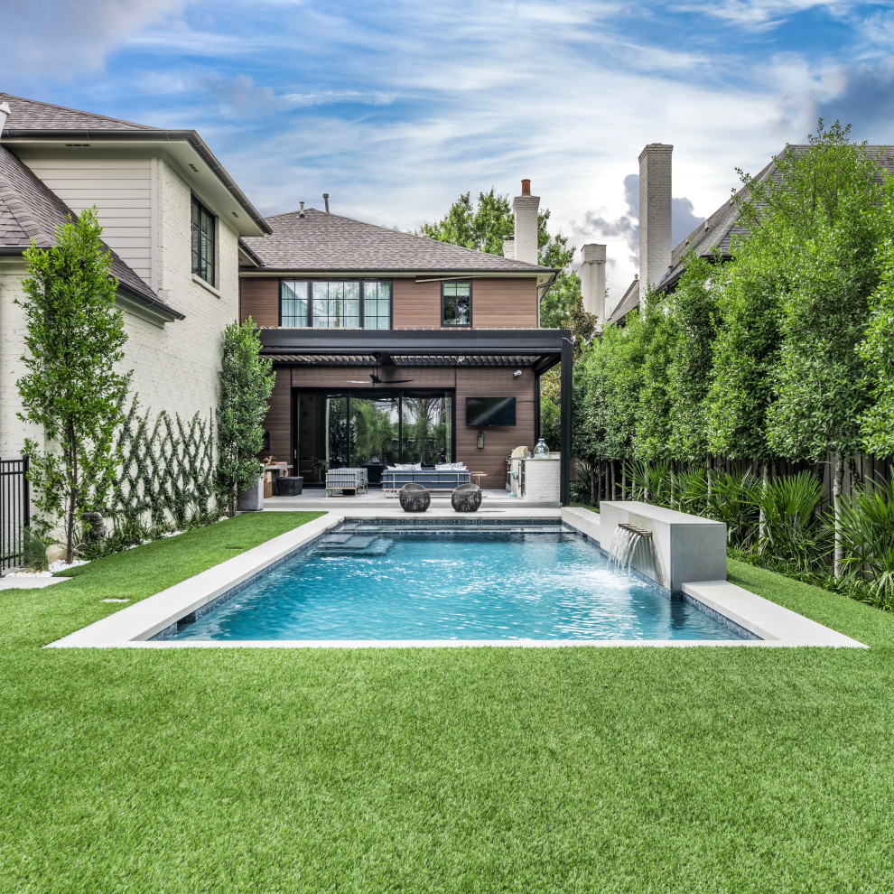 This is an example of a medium sized classic back rectangular swimming pool in Dallas with a water feature.