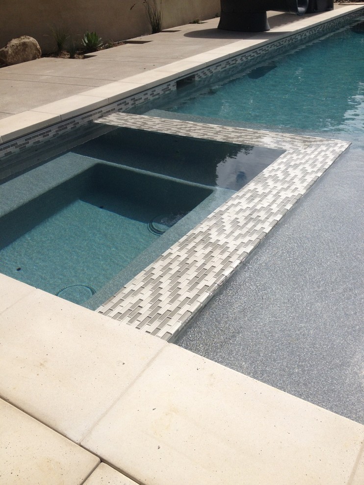 Esempio di una piscina monocorsia minimal rettangolare di medie dimensioni e dietro casa con una vasca idromassaggio e pavimentazioni in cemento