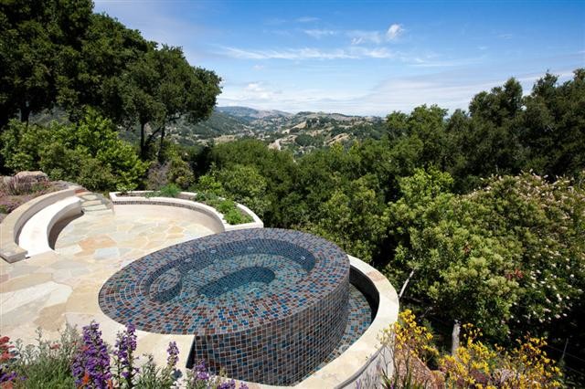 Aménagement d'une piscine à débordement et arrière méditerranéenne de taille moyenne et sur mesure avec des pavés en pierre naturelle et un bain bouillonnant.