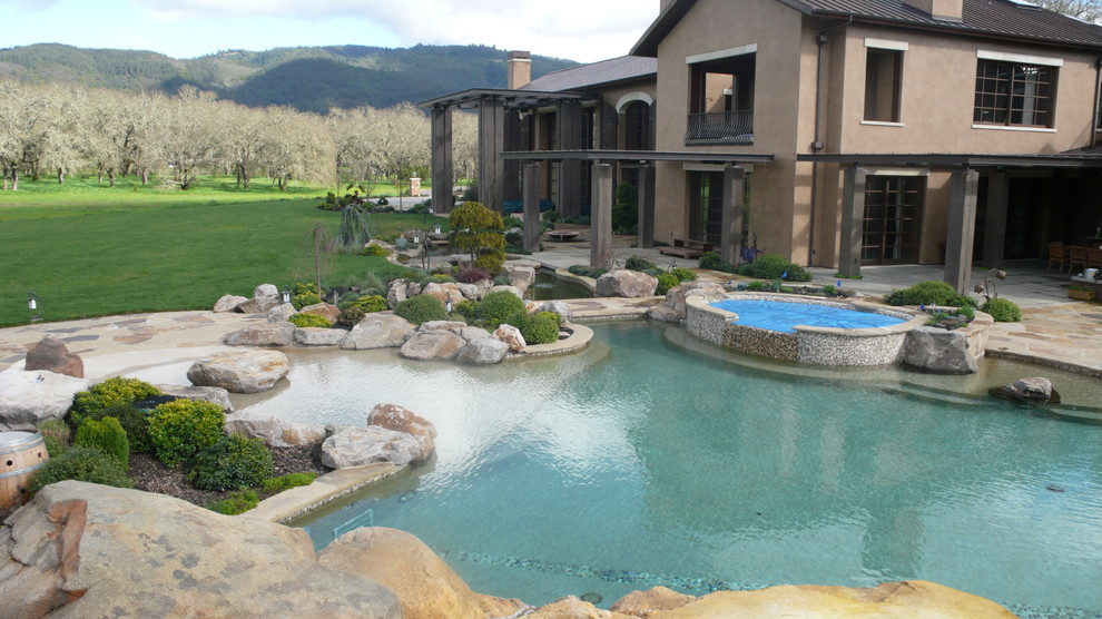 Aménagement d'une très grande piscine naturelle et arrière exotique sur mesure avec un bain bouillonnant et des pavés en pierre naturelle.