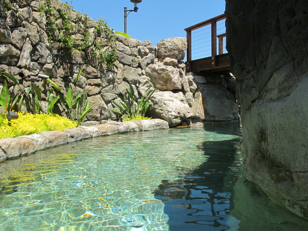 Foto på en stor tropisk baddamm på baksidan av huset, med naturstensplattor och vattenrutschkana