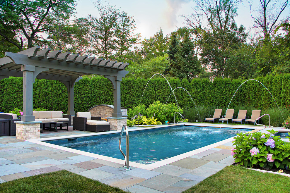 Klassischer Pool hinter dem Haus in rechteckiger Form mit Natursteinplatten und Wasserspiel in Chicago