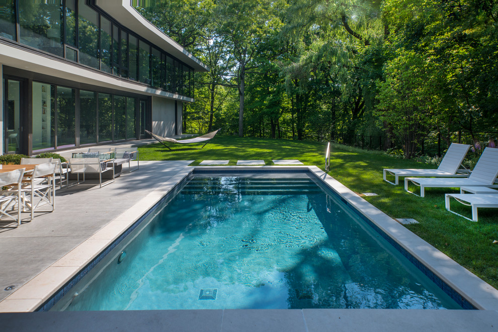 Modelo de piscina alargada moderna pequeña rectangular en patio trasero con adoquines de piedra natural