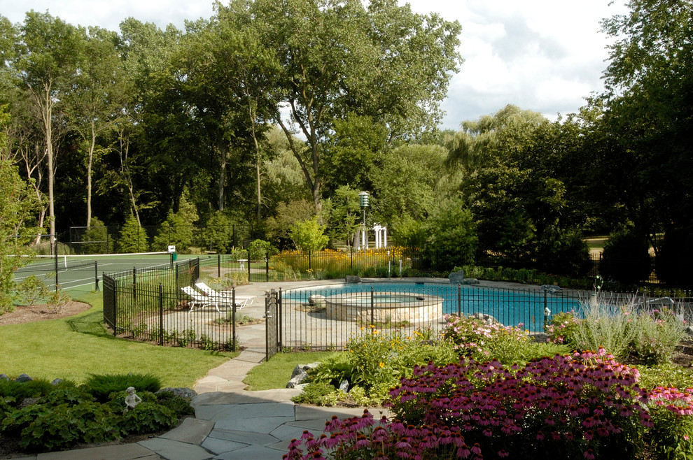 На фото: большой естественный бассейн на заднем дворе в стиле рустика с джакузи и покрытием из каменной брусчатки