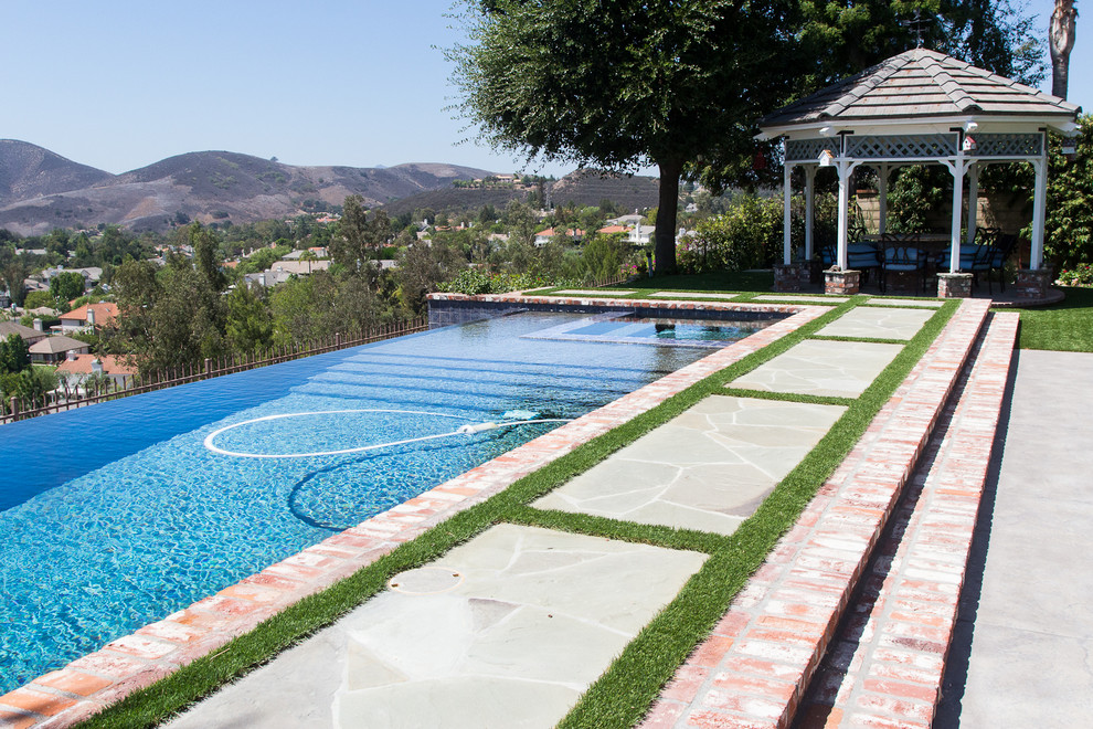 Mid-sized minimalist backyard brick and rectangular infinity pool fountain photo in Los Angeles