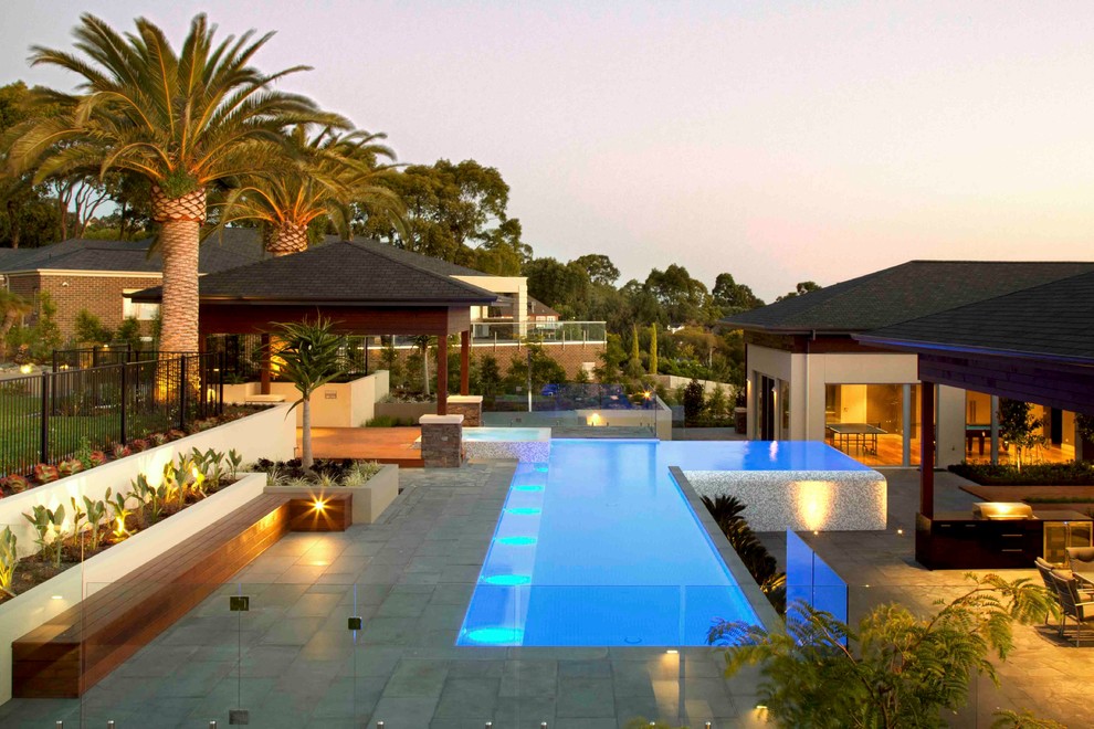 Imagen de piscina elevada actual en forma de L en patio trasero con adoquines de hormigón