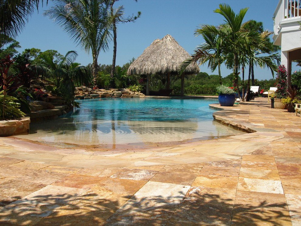 Ejemplo de piscina natural exótica grande a medida en patio trasero con adoquines de piedra natural
